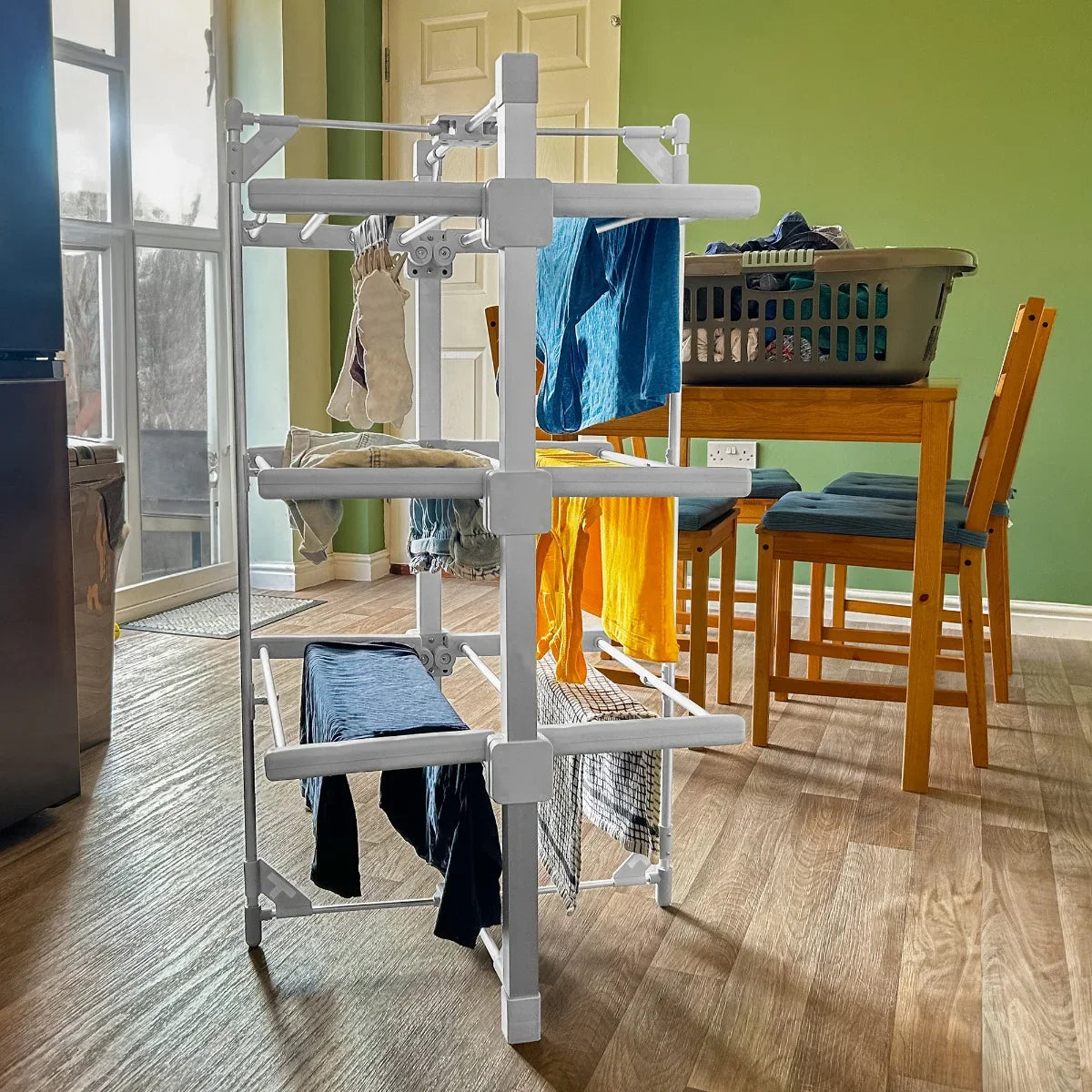 Heated clothes airer with multiple tiers, featuring white plastic frame and drying clothes in various colors, set in a bright room