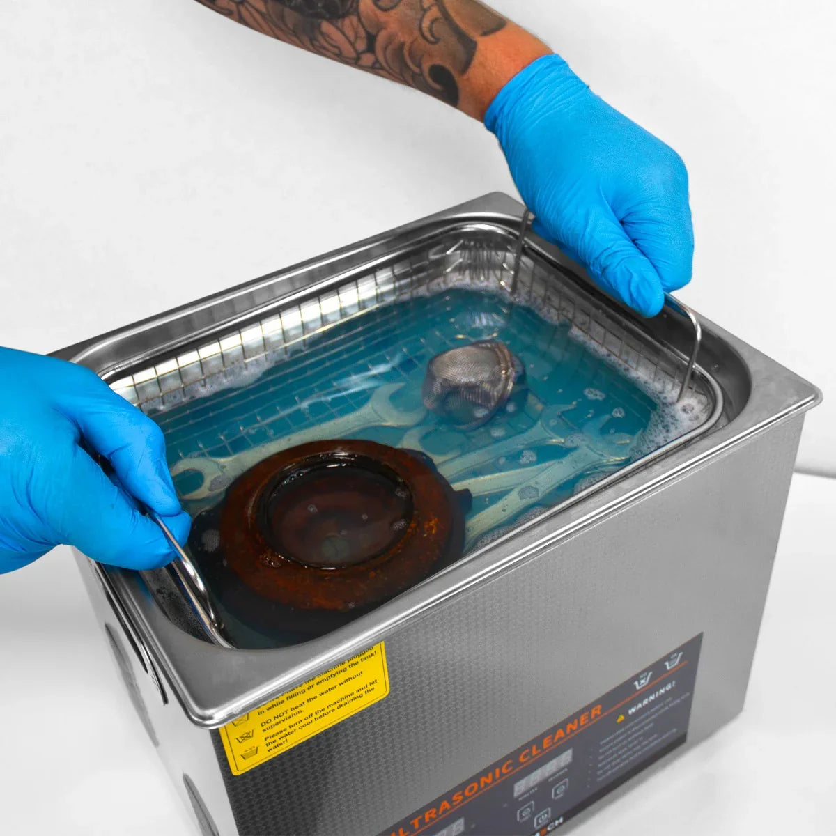 T-Mech Ultrasonic Cleaner 10L with blue liquid, stainless steel tank, and a hand wearing a blue glove holding a metal basket