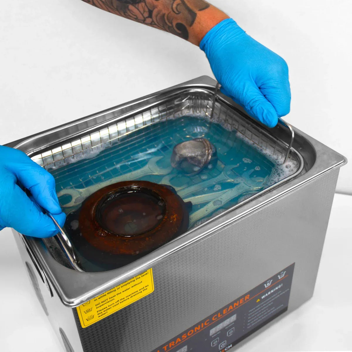T-Mech Ultrasonic Cleaner 15L with stainless steel tank, blue cleaning solution, and a hand gripping the metal handles