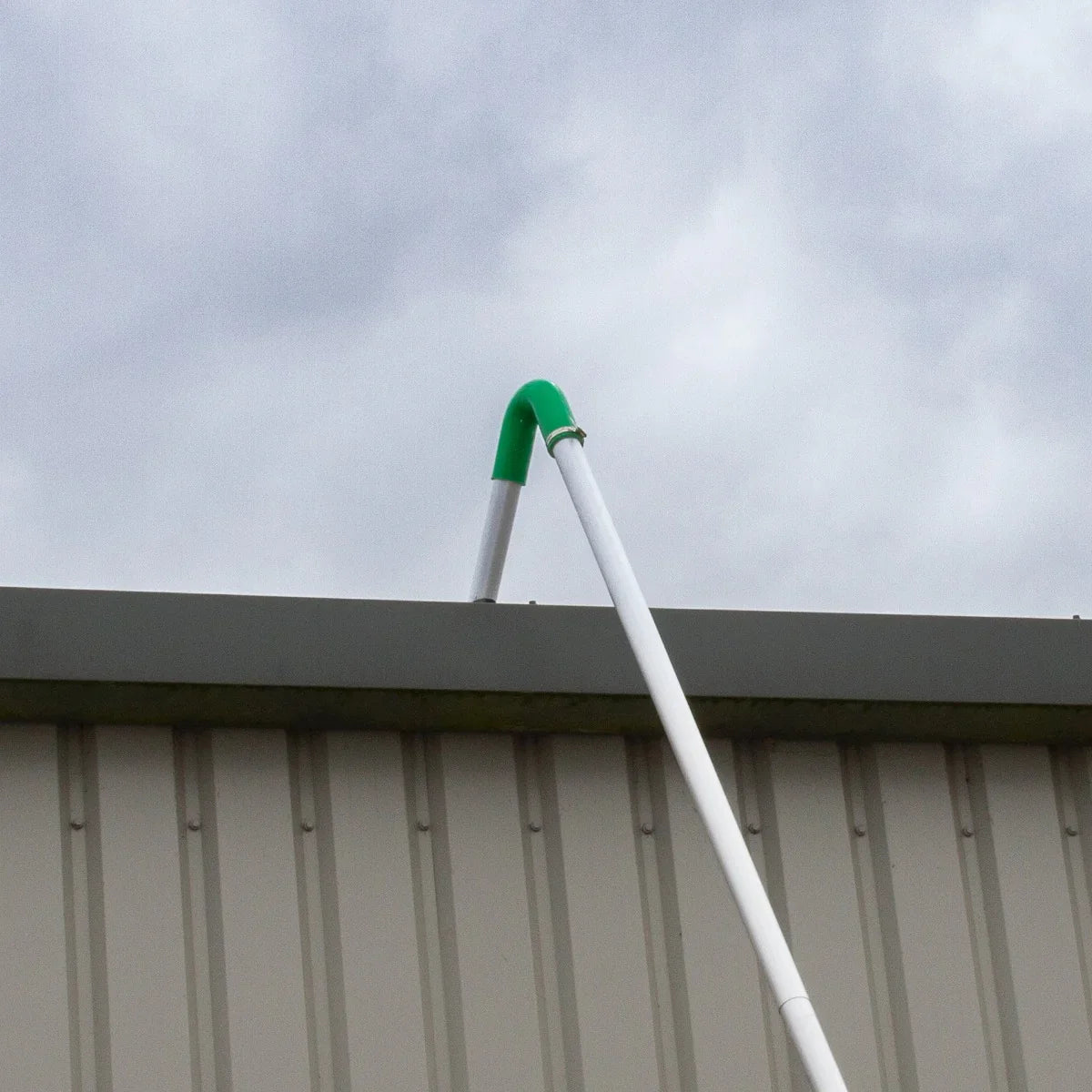 Maxblast Gutter Vacuum Poles 7.2m in white with a green curved end, extending over a building's edge against a cloudy sky