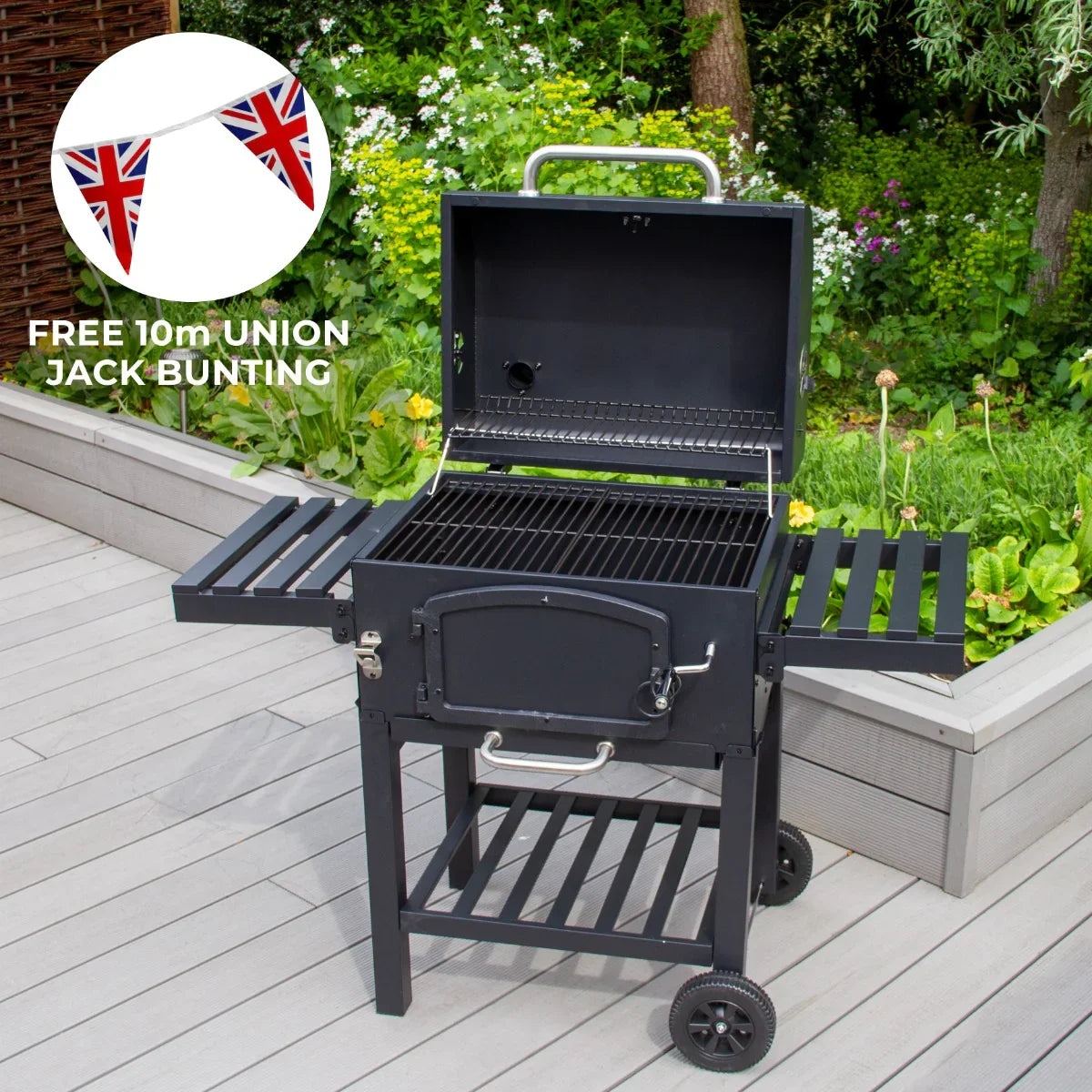 XL BBQ smoker grill in black with open lid, side shelves, and free 10m Union Jack bunting, set on a wooden deck with greenery