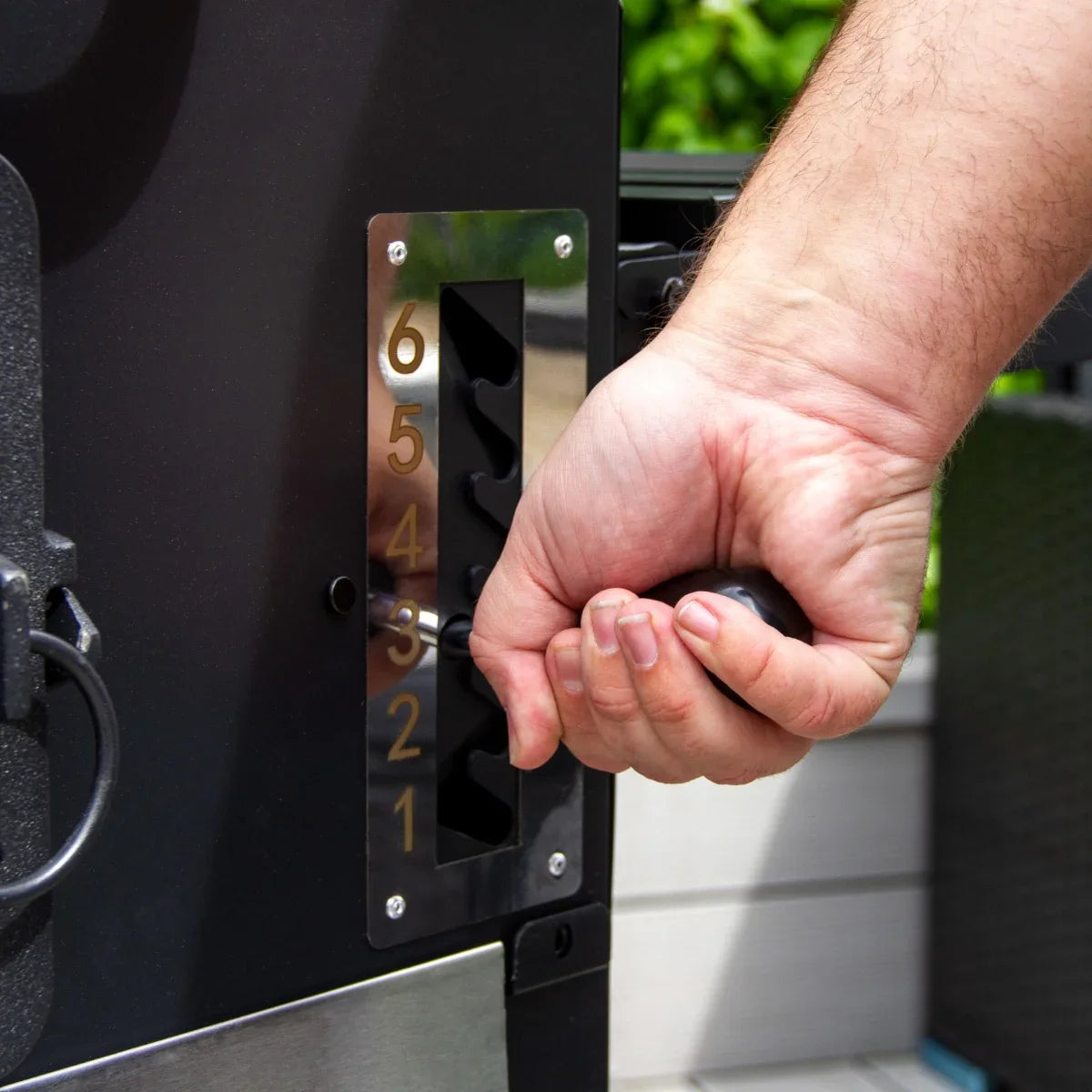 Hand adjusting the temperature gauge on the XXL BBQ Smoker Grill, featuring a sleek black finish and stainless steel accents