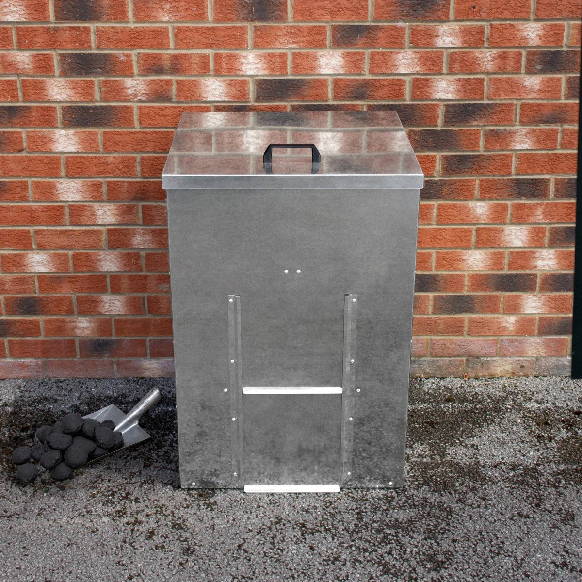 Galvanised coal bunker with a sturdy metal construction, featuring a flat lid, handle, and a textured finish, beside a shovel and coal pile