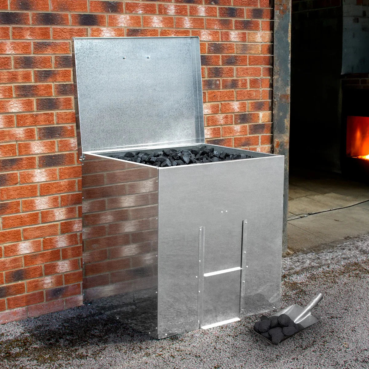 Galvanised coal bunker with a shiny metallic finish, holding 250kg of coal, set against a brick wall and gravel surface