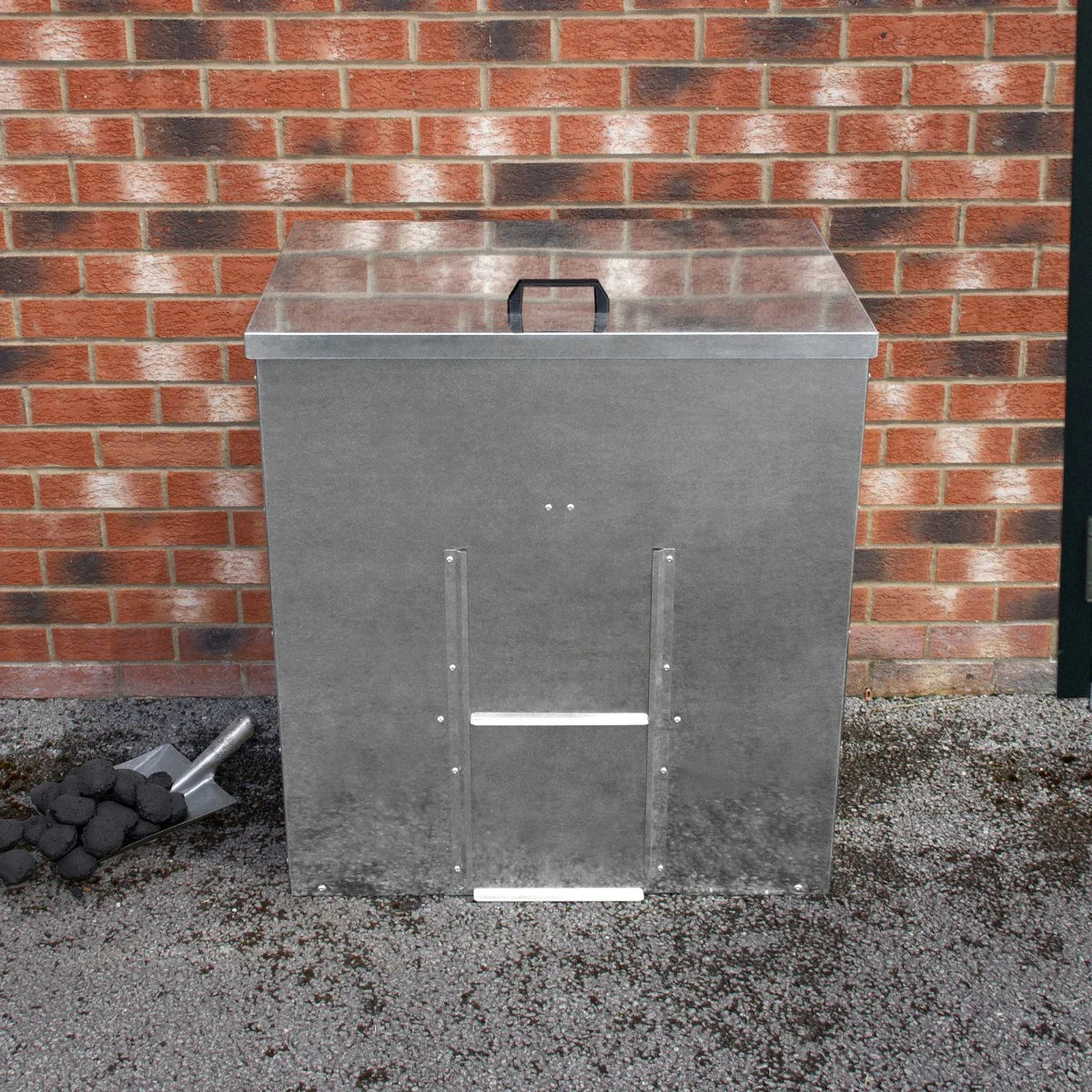 Galvanised coal bunker for 250kg storage, featuring a sturdy metal design, flat lid, and side access panel, placed against a brick wall