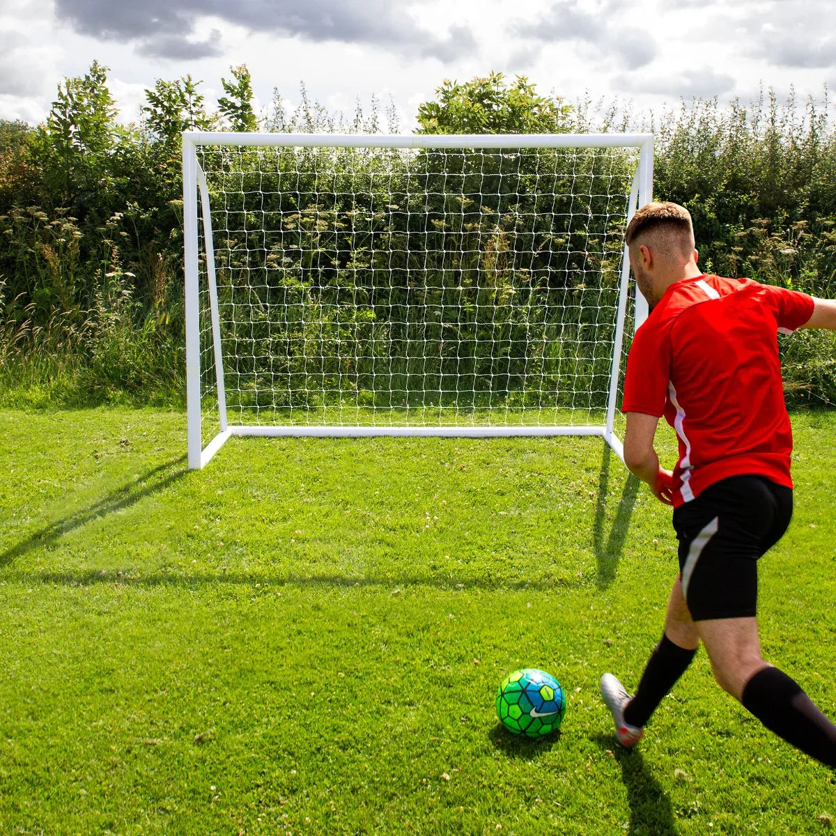 8 x 6ft football goal with white frame and net, set on green grass, as a player in red kicks a colorful soccer ball towards it