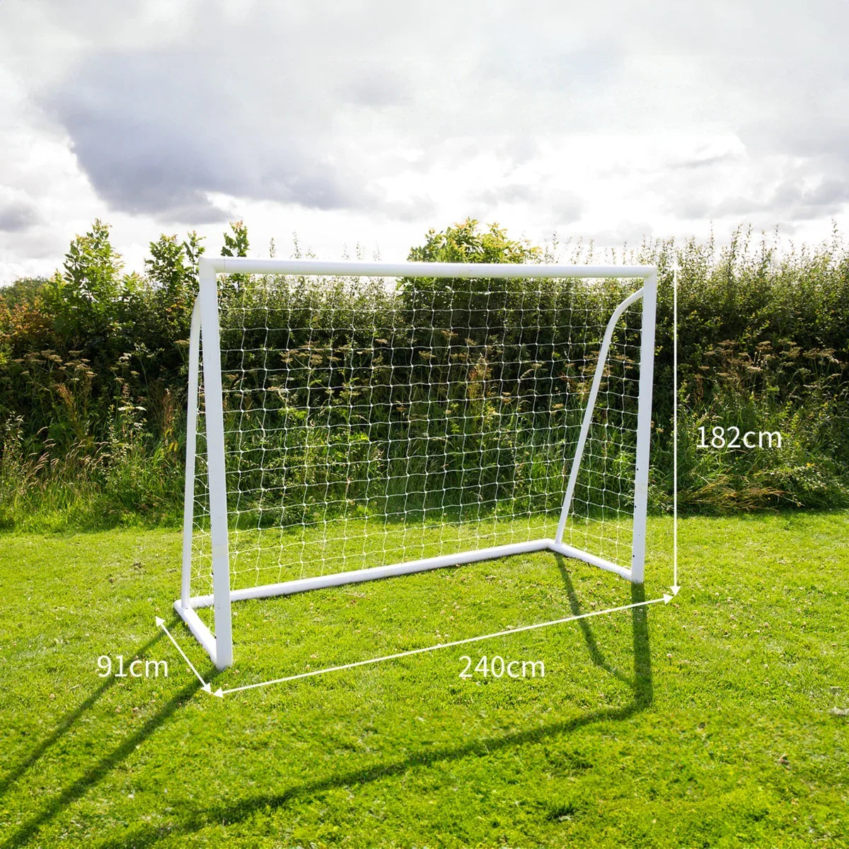 8 x 6ft white football goal with net, set on grass, dimensions marked, surrounded by greenery and cloudy sky in the background