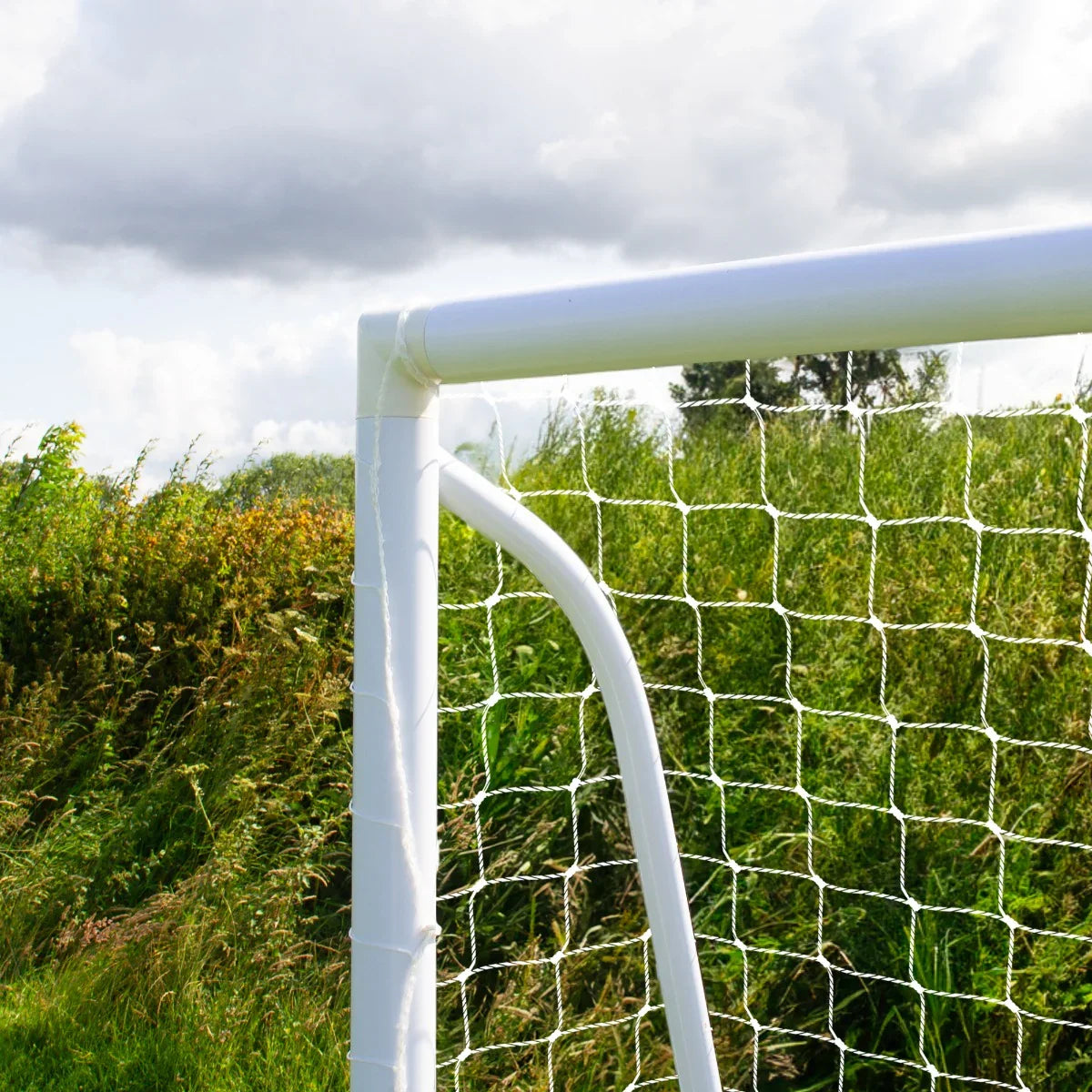 White PVC football goal corner with netting, set against a grassy field and cloudy sky, showcasing sturdy construction...