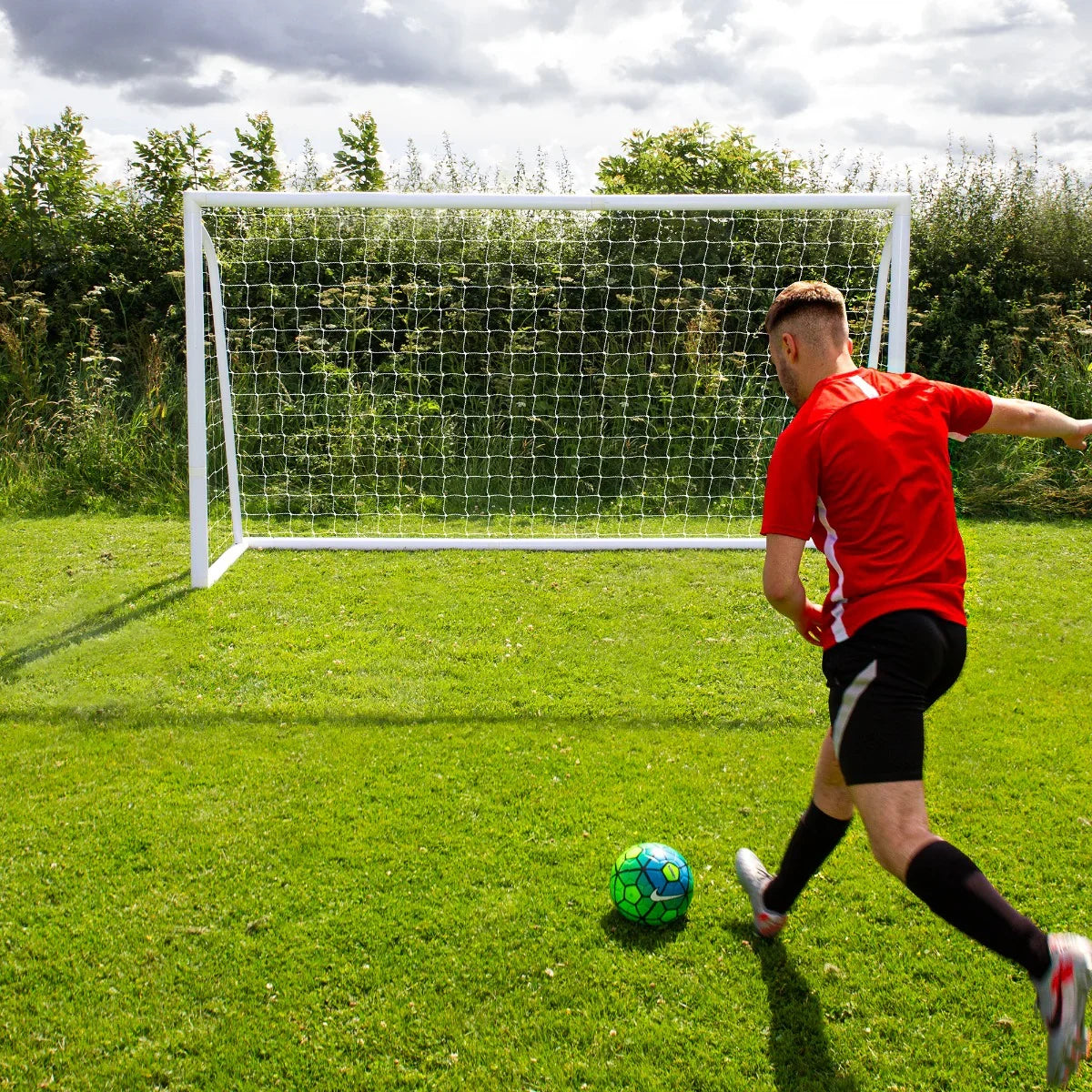 12 x 6ft white football goal on grass, player in red shirt kicking a green soccer ball towards the net under cloudy sky