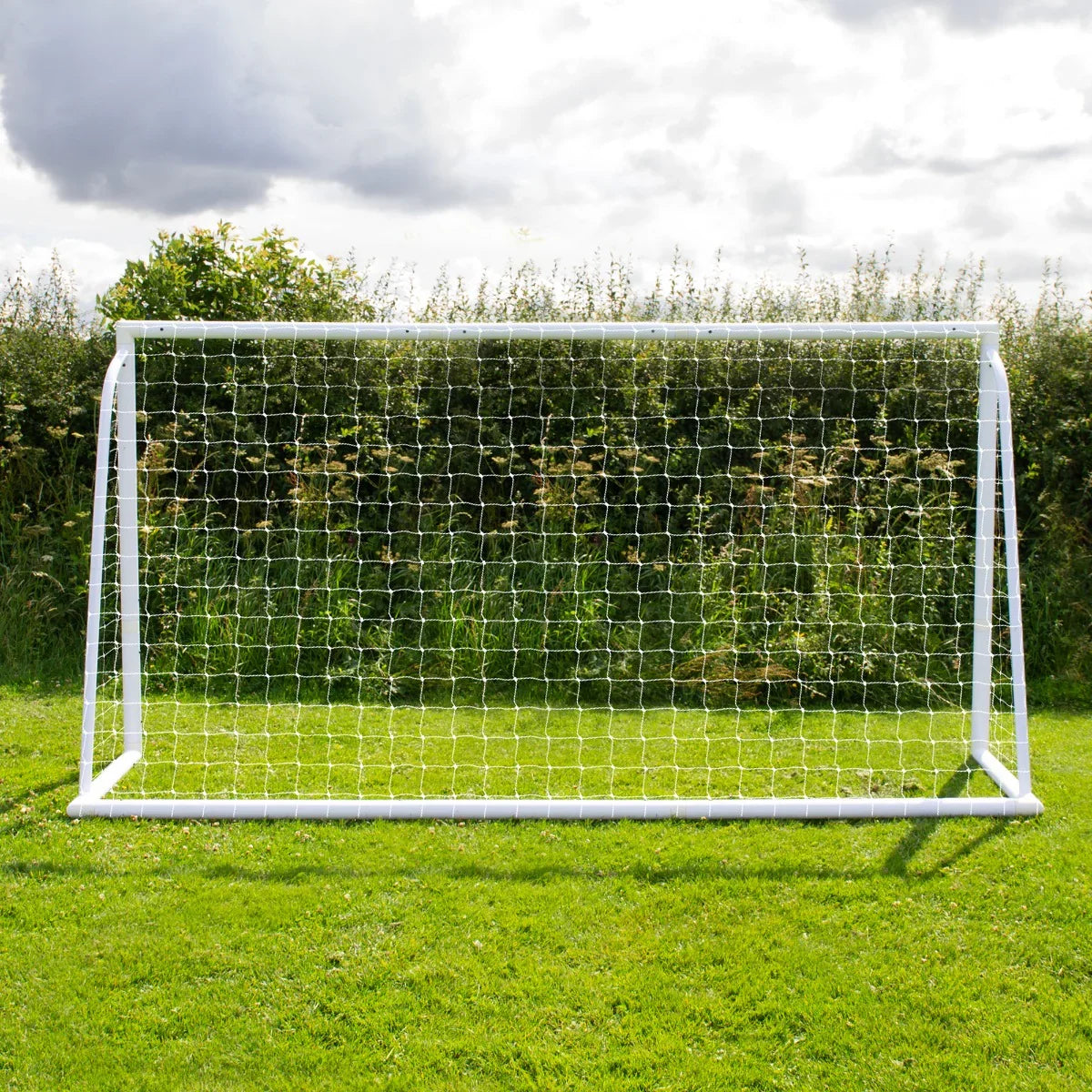 12 x 6ft white football goal with netting, set on green grass, surrounded by tall grass and a cloudy sky backdrop