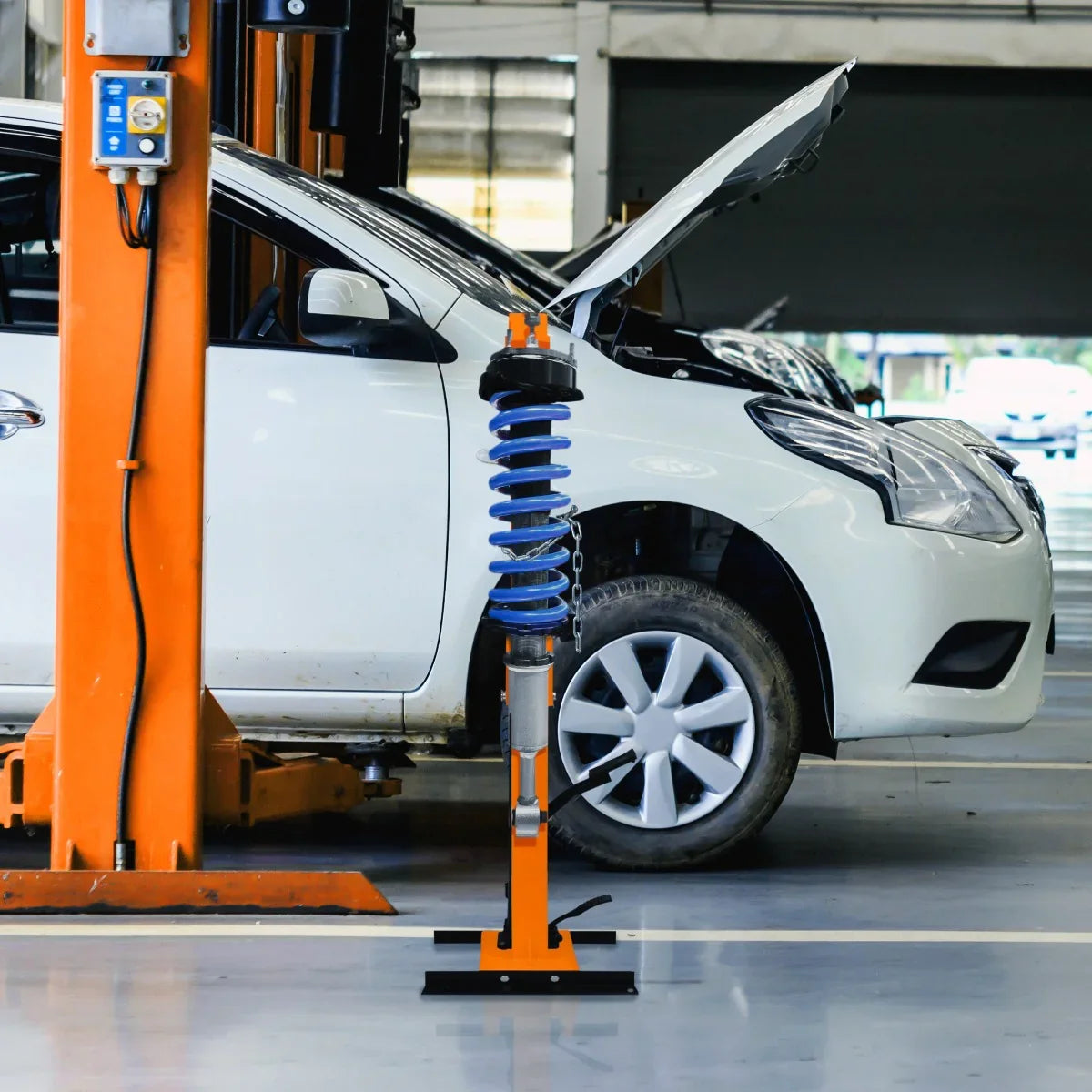 Hydraulic Coil Spring Strut 3T in bright orange and blue, positioned beside a white car in a garage with an open hood