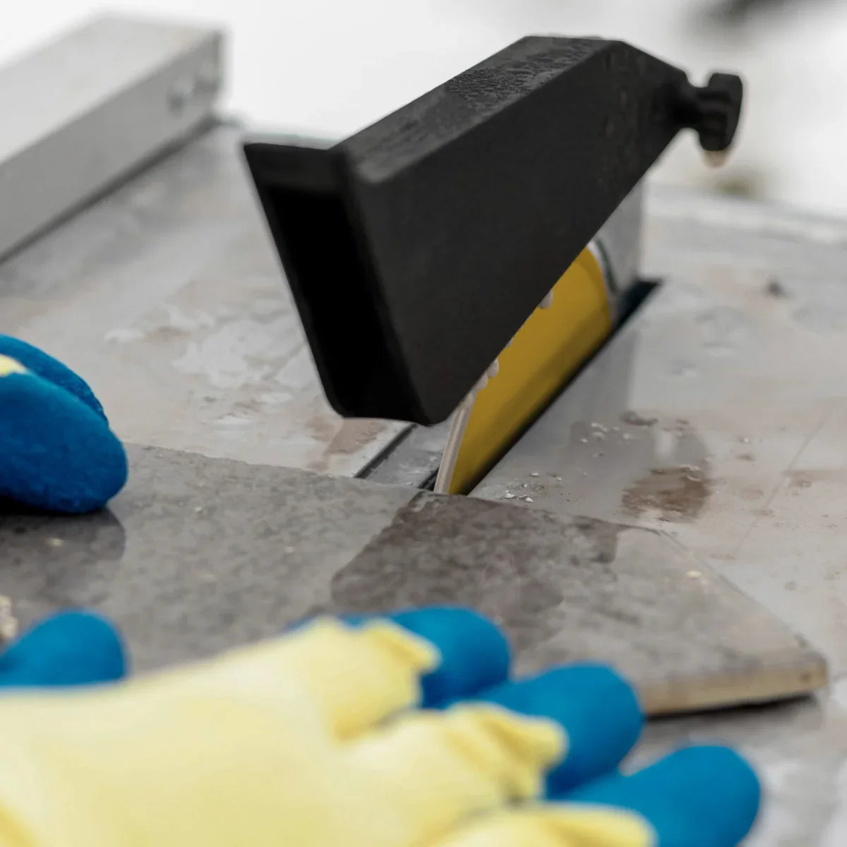 T-Mech Electric Wet Tile Cutter 600W with a sharp blade cutting through a gray tile, featuring protective gloves nearby