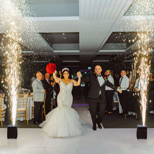 Bride in a stunning mermaid gown and groom joyfully enter a wedding reception, surrounded by sparklers and elegant decor