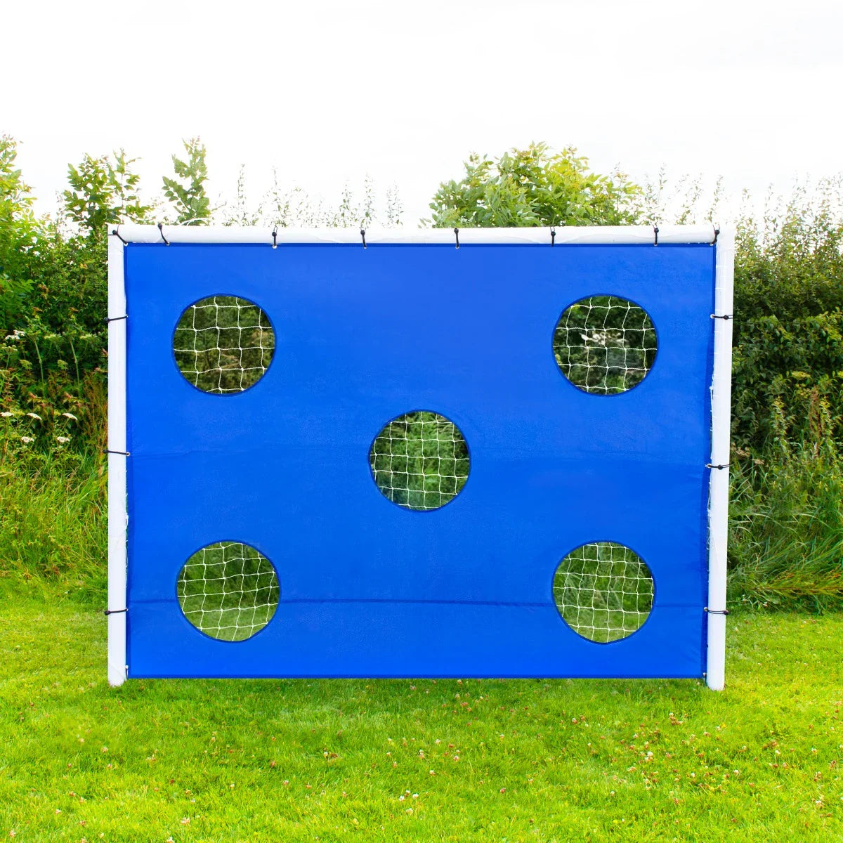 Bright blue 8 x 6ft football goal target sheet with five circular netted holes, designed for skill practice in grassy outdoor settings