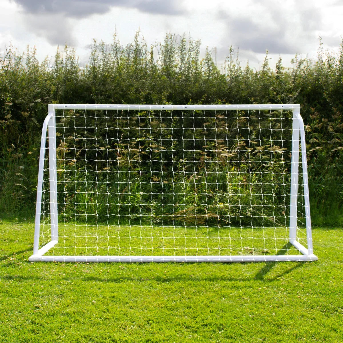 6 x 4ft football goal with white frame and netting, set on green grass, surrounded by lush greenery under a cloudy sky