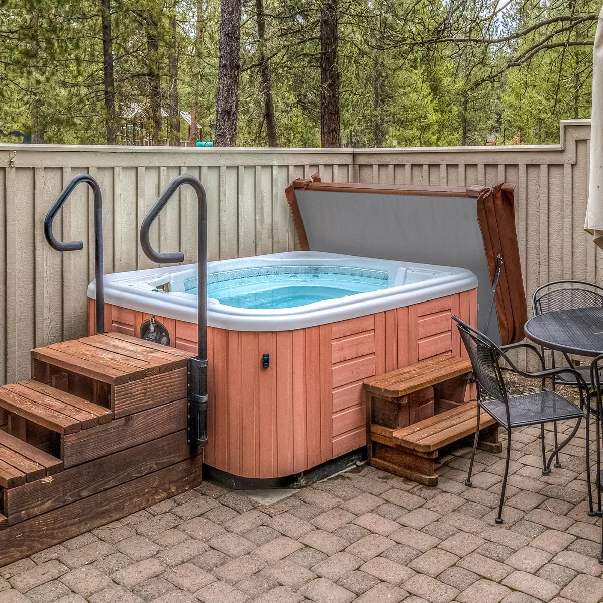 Brown 2m hot tub spa cover partially open, revealing a turquoise water-filled spa, surrounded by wooden steps and patio furniture