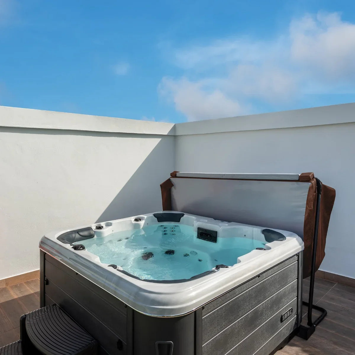 Brown 2m hot tub spa cover resting on a modern hot tub, showcasing a sleek design against a clear blue sky and white wall