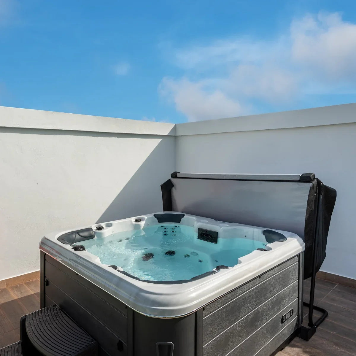 Black 2m hot tub spa cover partially open, showcasing the bubbling water inside and sleek design against a clear blue sky