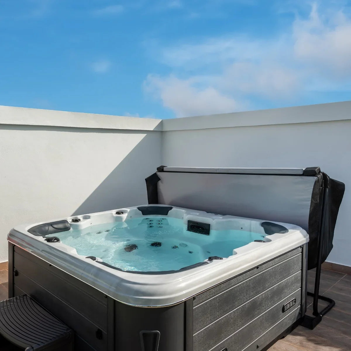 Black 2.2m hot tub spa cover partially open, revealing a clear water-filled spa with jets, set against a bright blue sky