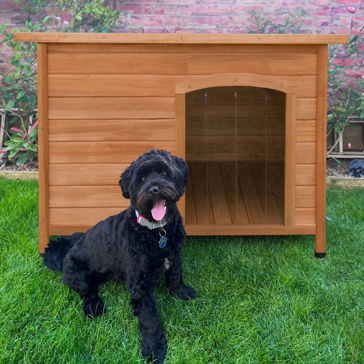 Medium wooden dog kennel with a slanted roof, featuring a cozy entrance, set on green grass with a happy black dog in front