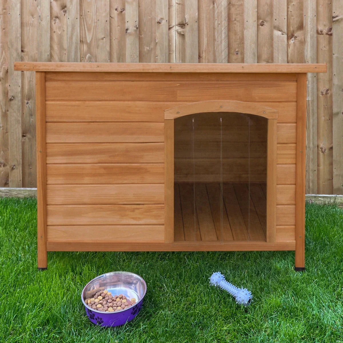 Medium wooden dog kennel with a slanted roof, natural finish, open front, placed on grass beside a food bowl and toy