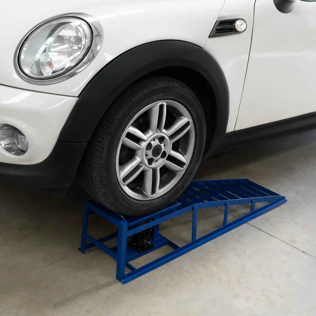 Hydraulic car ramps in blue support a vehicle's front tire, showcasing sturdy metal construction and a sloped design for easy access