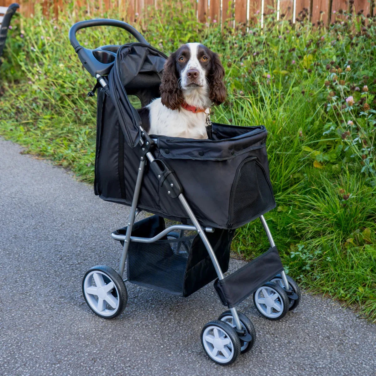 Black pet stroller with rain cover, featuring a spacious mesh-lined interior, sturdy wheels, and a comfortable seated dog inside