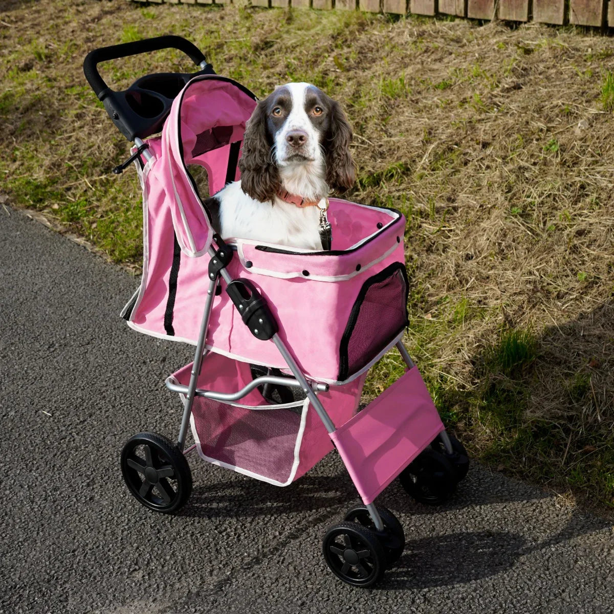 Pink pet stroller with rain cover, featuring a spacious mesh-lined compartment, sturdy wheels, and a happy dog inside