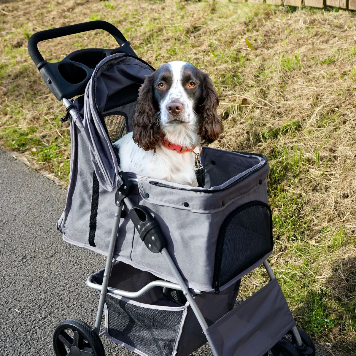 Grey pet stroller with rain cover, featuring a spacious cabin and mesh windows, comfortably carrying a dog on a sunny path