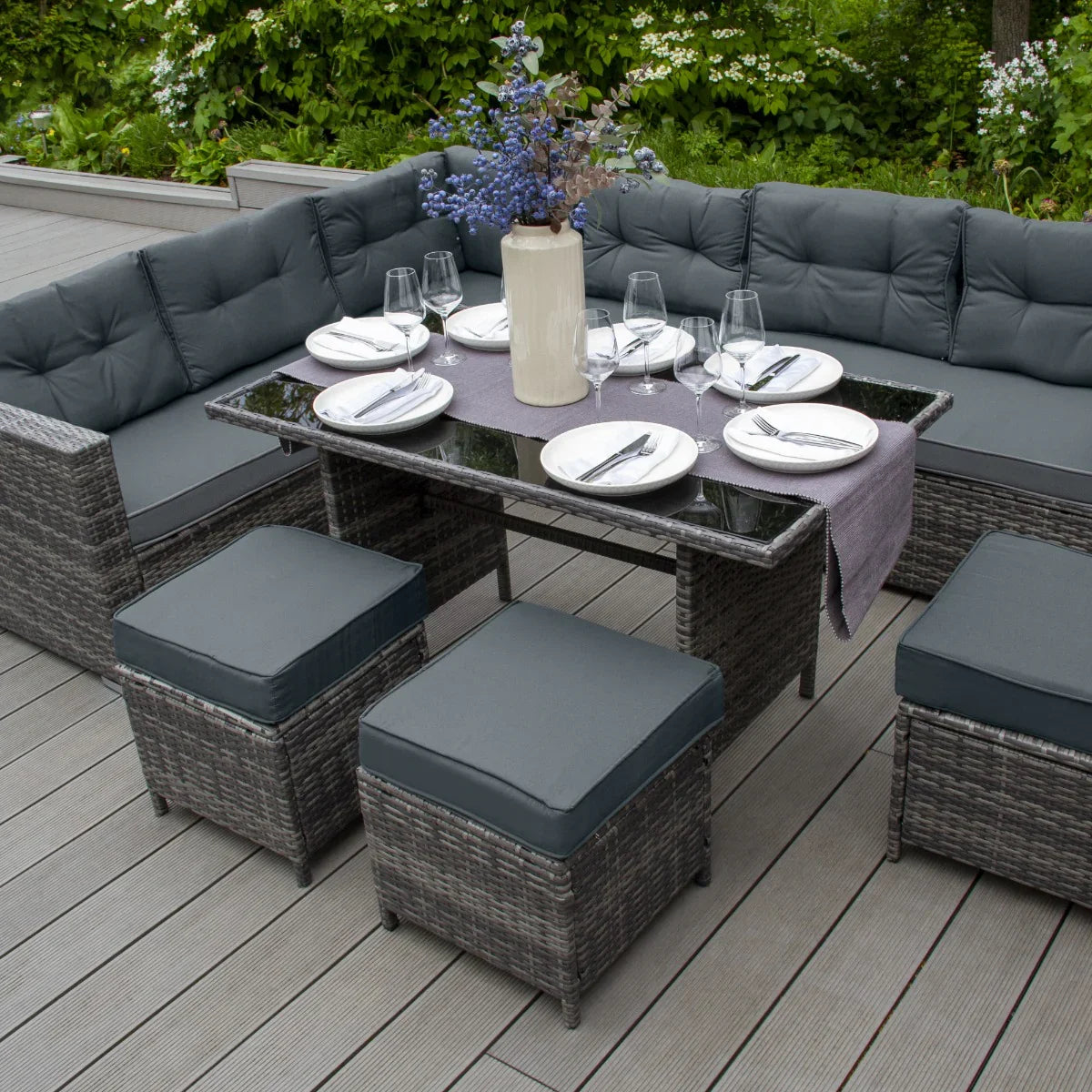 Grey rattan corner set featuring plush cushions, a glass-topped table, and stylish stools, perfect for outdoor dining and relaxation