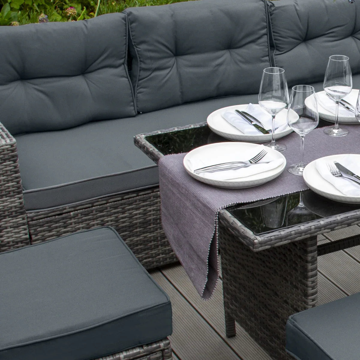 Grey rattan corner set featuring plush cushions, a glass tabletop, and elegant dinnerware, perfect for outdoor dining and relaxation