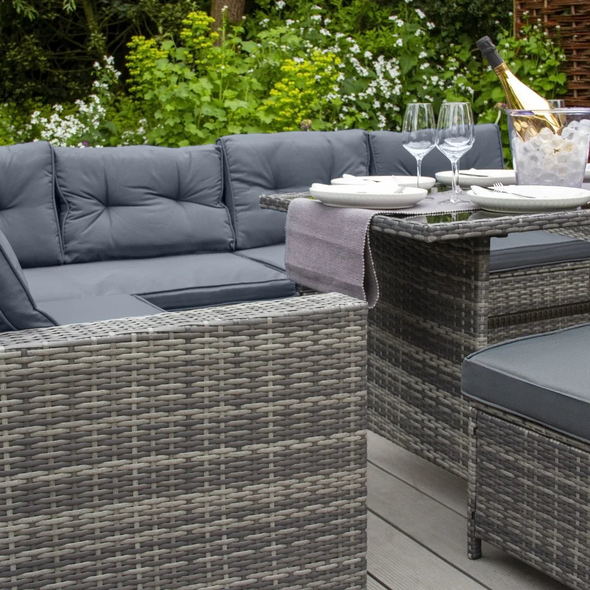 Grey rattan corner set featuring plush cushions, a glass-top table, and elegant outdoor decor, perfect for garden lounging