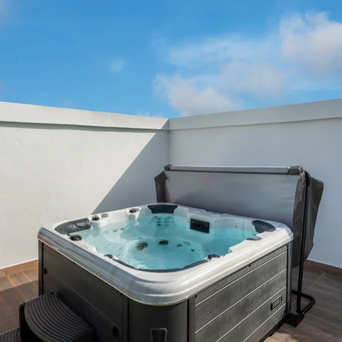 Grey 2m hot tub spa cover partially open, revealing bubbling water and black textured exterior, set against a clear blue sky