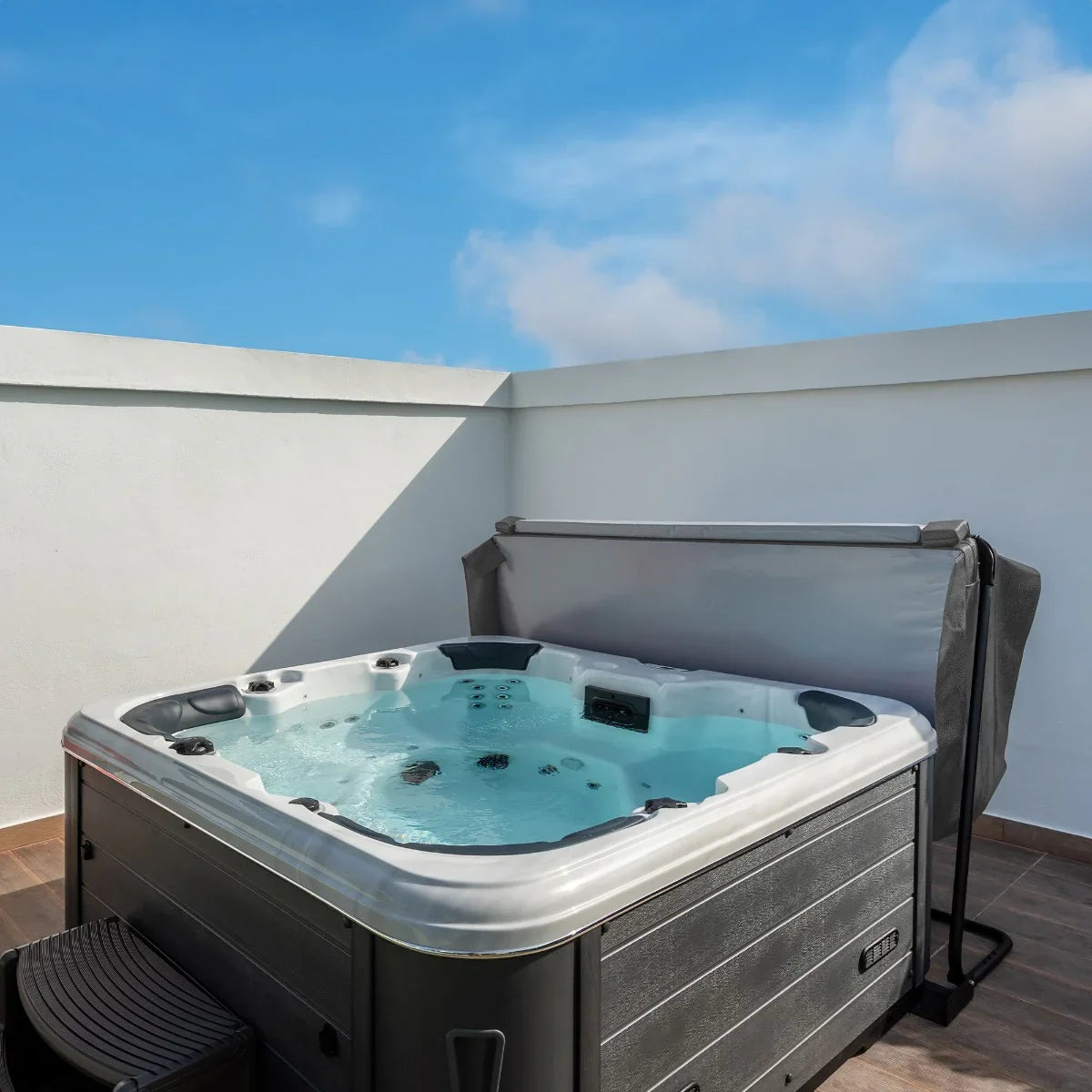 Grey 2.1m hot tub spa cover partially open, showcasing the water and jets inside, set against a clear blue sky and white wall