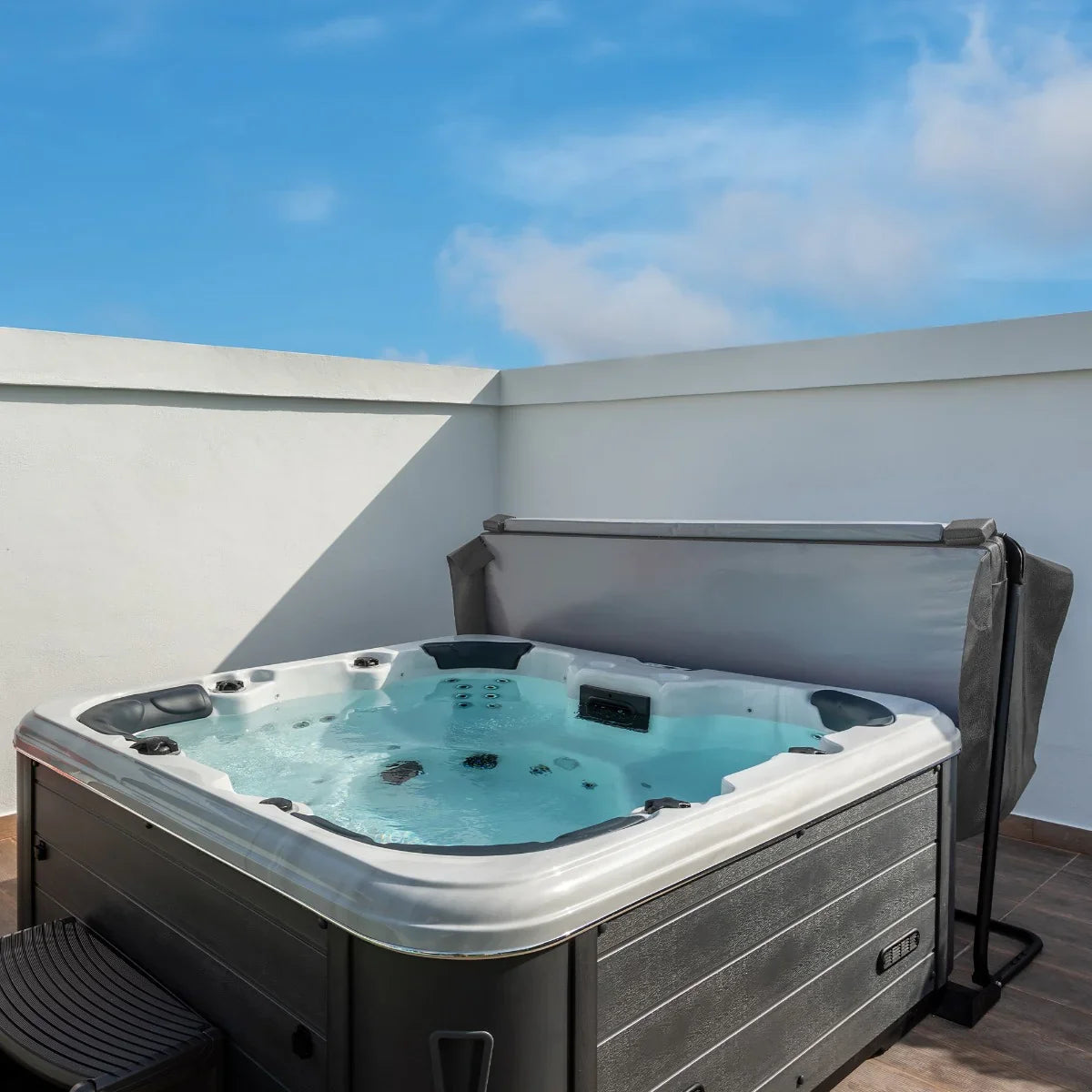 Grey 2.2m hot tub spa cover partially open, revealing bubbling water and sleek design, set against a clear blue sky and white wall
