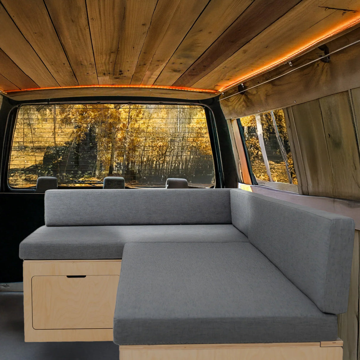 L-shaped camper van bed with gray upholstery, wooden accents, and cozy seating, perfect for van life adventures and comfort