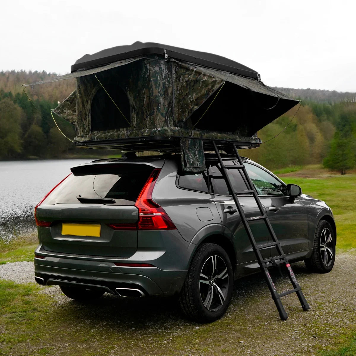 Camouflage car roof tent mounted on a sleek SUV, featuring a sturdy ladder and a scenic lakeside backdrop with trees
