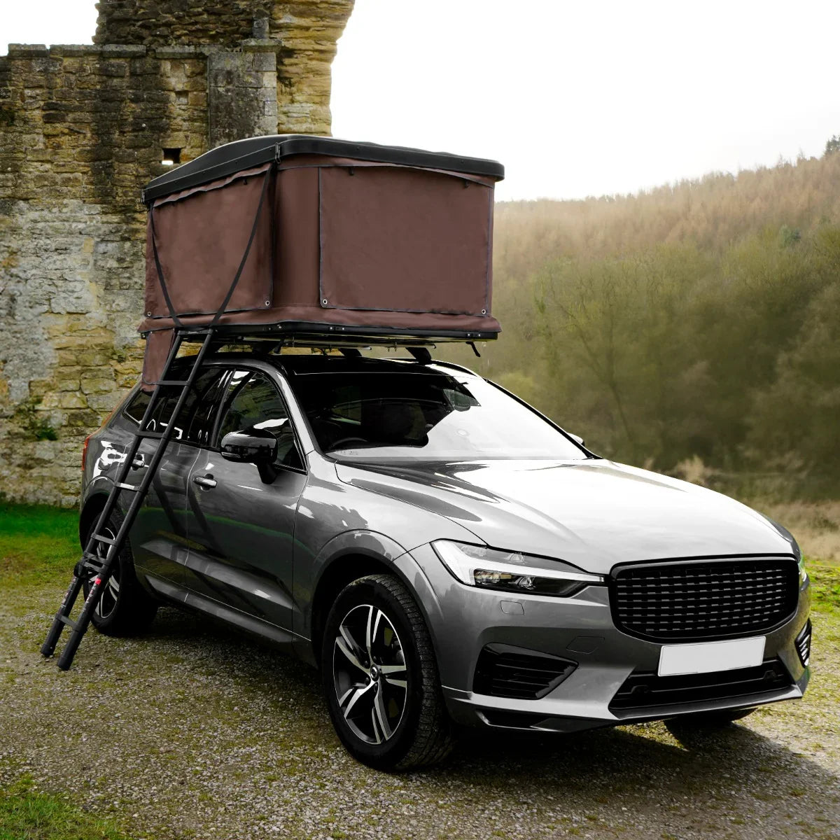 Brown car roof tent mounted on a sleek silver SUV, featuring a sturdy frame and ladder, set against a scenic outdoor backdrop