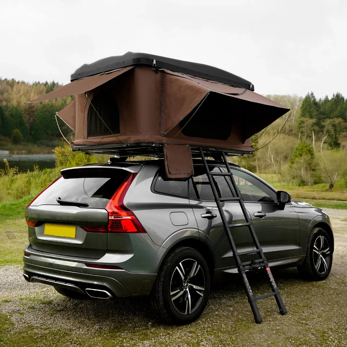 Brown car roof tent mounted on a silver SUV, featuring spacious openings, a sturdy ladder, and a scenic outdoor backdrop