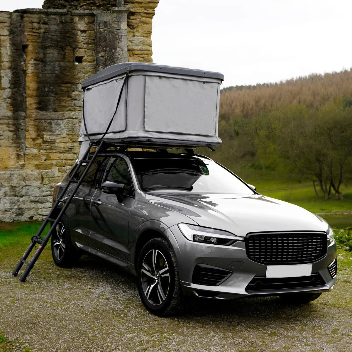 Grey car roof tent mounted on a sleek silver SUV, featuring sturdy poles and a spacious, weather-resistant design in a scenic outdoor setting