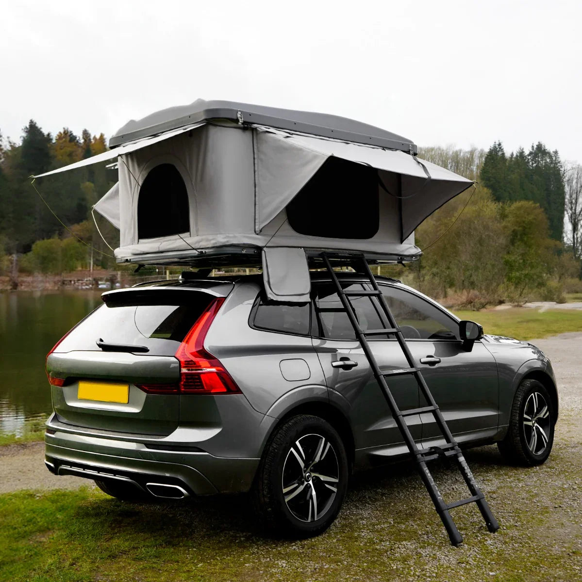 Grey car roof tent mounted on a sleek SUV, featuring spacious openings, a sturdy ladder, and a scenic lakeside backdrop