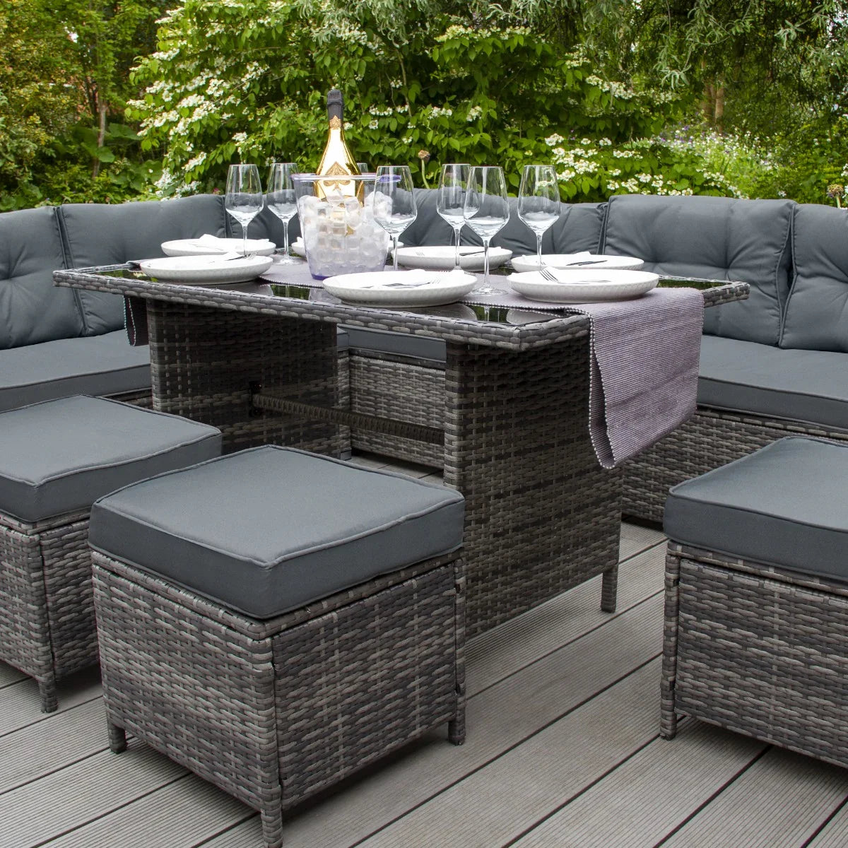 Grey rattan corner set with plush cushions, a central storage box, and a stylish dining setup featuring plates and glasses outdoors