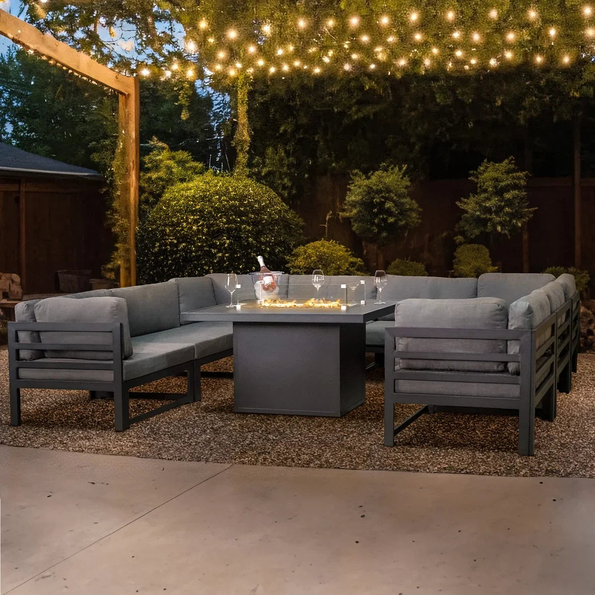 Modular garden furniture set in anthracite grey with plush cushions, featuring a central fire pit, surrounded by twinkling lights and greenery