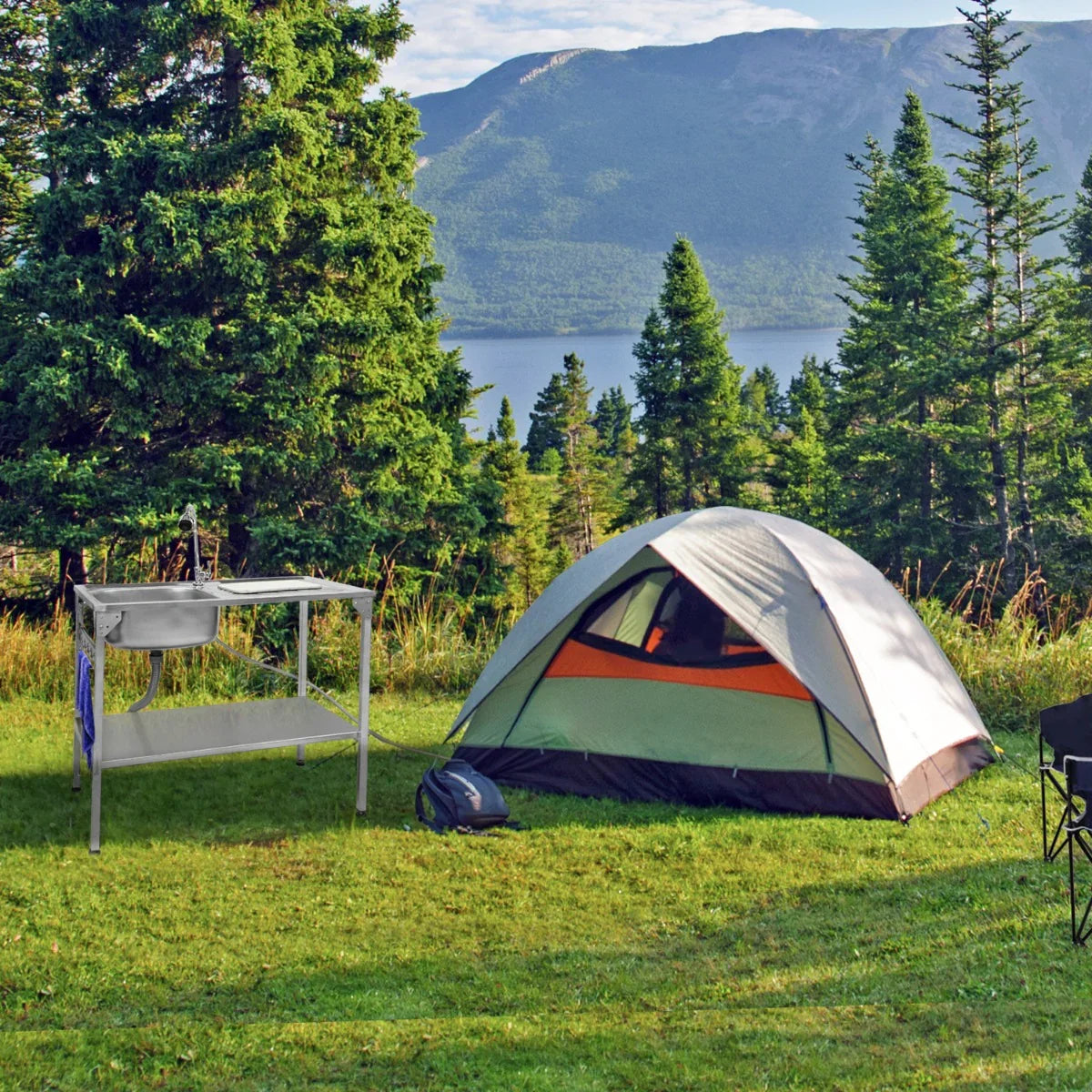 Folding camping sink with a stainless steel basin on a sturdy frame, set in a scenic outdoor campsite near a lake and trees