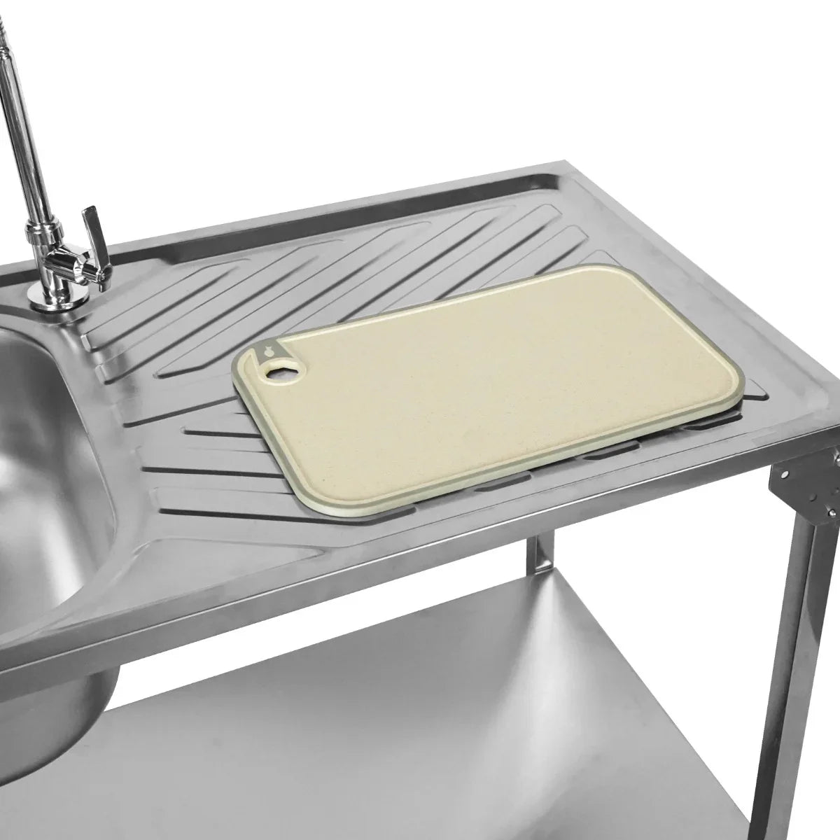 Folding camping sink with a sleek stainless steel basin, featuring a beige cutting board on a textured surface for easy food prep