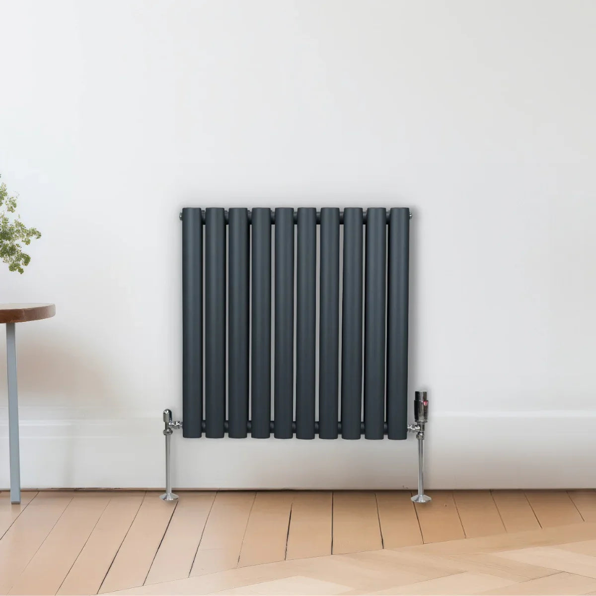 Anthracite grey oval column radiator with vertical slats, sleek design, and chrome valves, mounted on a light wooden floor