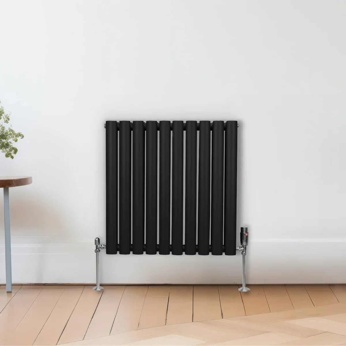 Sleek black oval column radiator, 600mm x 600mm, mounted on a white wall, with polished metal feet and a modern design