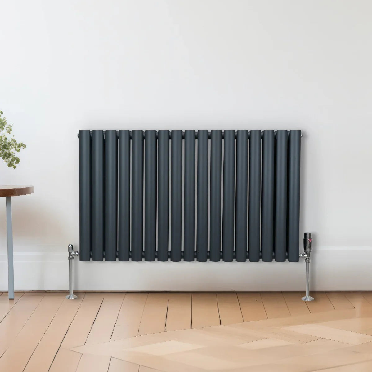 Oval column radiator in anthracite grey, featuring vertical bars and a sleek design, mounted on the wall with visible valves