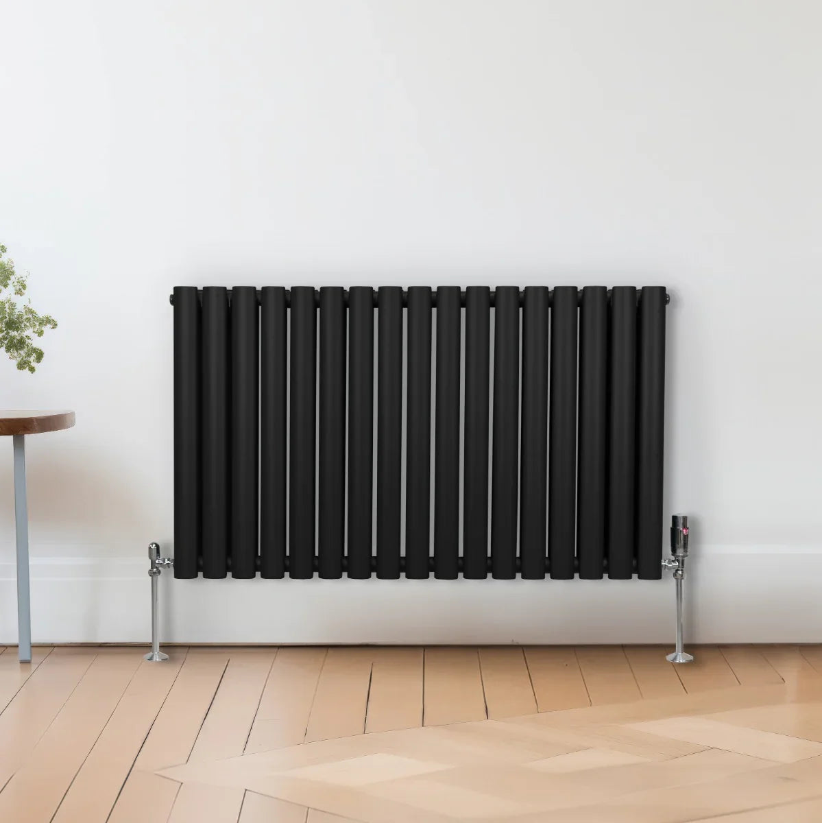 Sleek black oval column radiator, 600mm x 1020mm, featuring vertical bars and a modern design, mounted on silver feet against a light wall