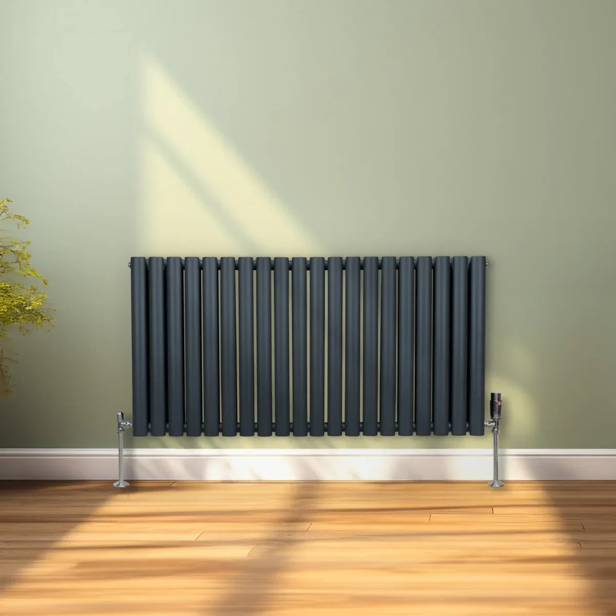 Oval column radiator in anthracite grey, featuring vertical bars and a sleek design, mounted against a light green wall in a cozy room